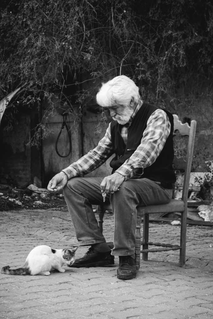 A heartfelt black and white photo of a senior man feeding a cat outdoors, capturing a moment of connection.